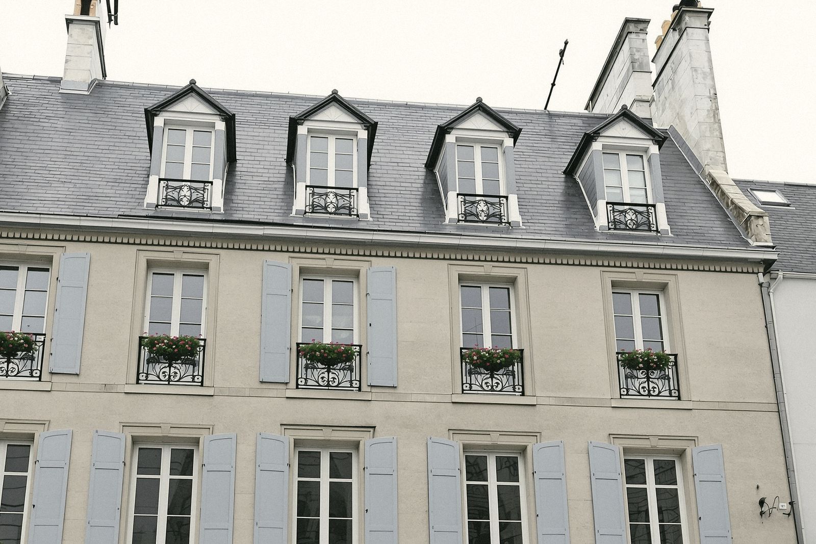Façade en pierre de taille à volets gris et toit en ardoise d'un hôtel de centre-ville