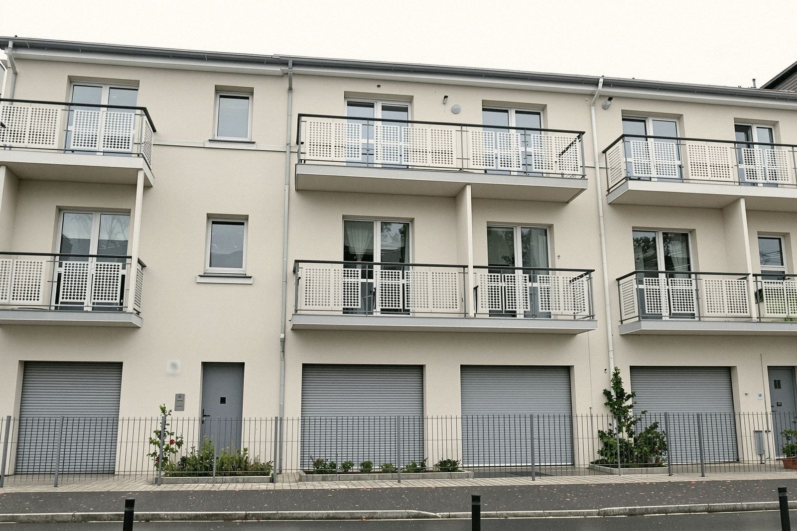 Petit immeuble résidentiel neuf en enduit clair avec balcons et volets roulants gris